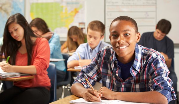 Portrait Of Male Pupil Studying At Desk In Classroom Looking To Camera Smiling