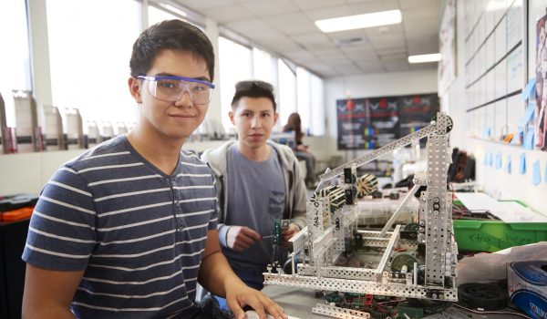Portrait Of Two Male College Students Building Machine In Science Robotics Or Engineering Class